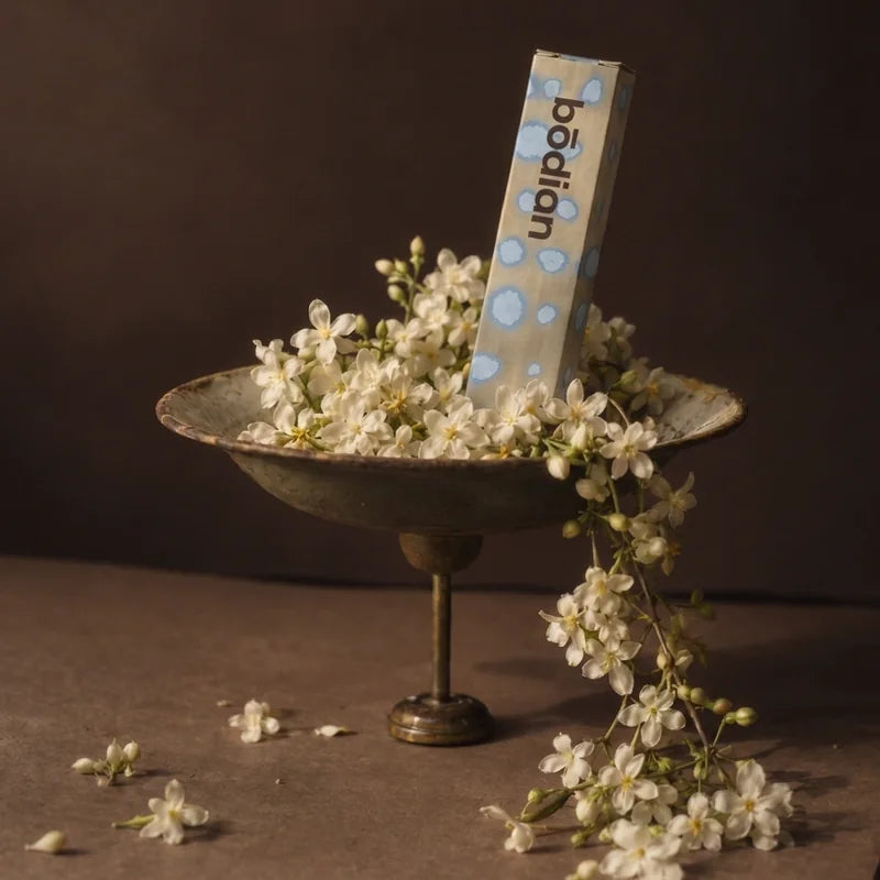 The bōdian carton standing in a pedestal dish of jasmine flowers, on brown paper