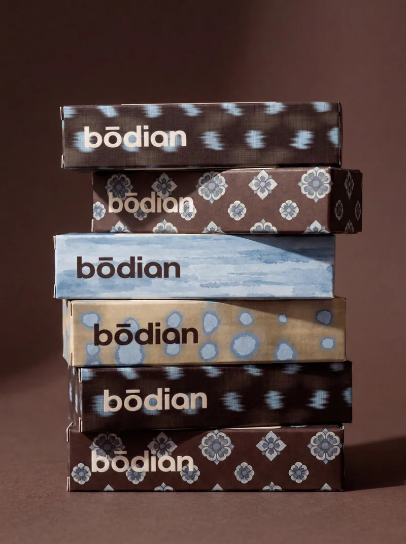 Six bōdian cartons stacked on a coffee-brown table, in ikat, treasure-flower, watercolour and plaster-dot prints